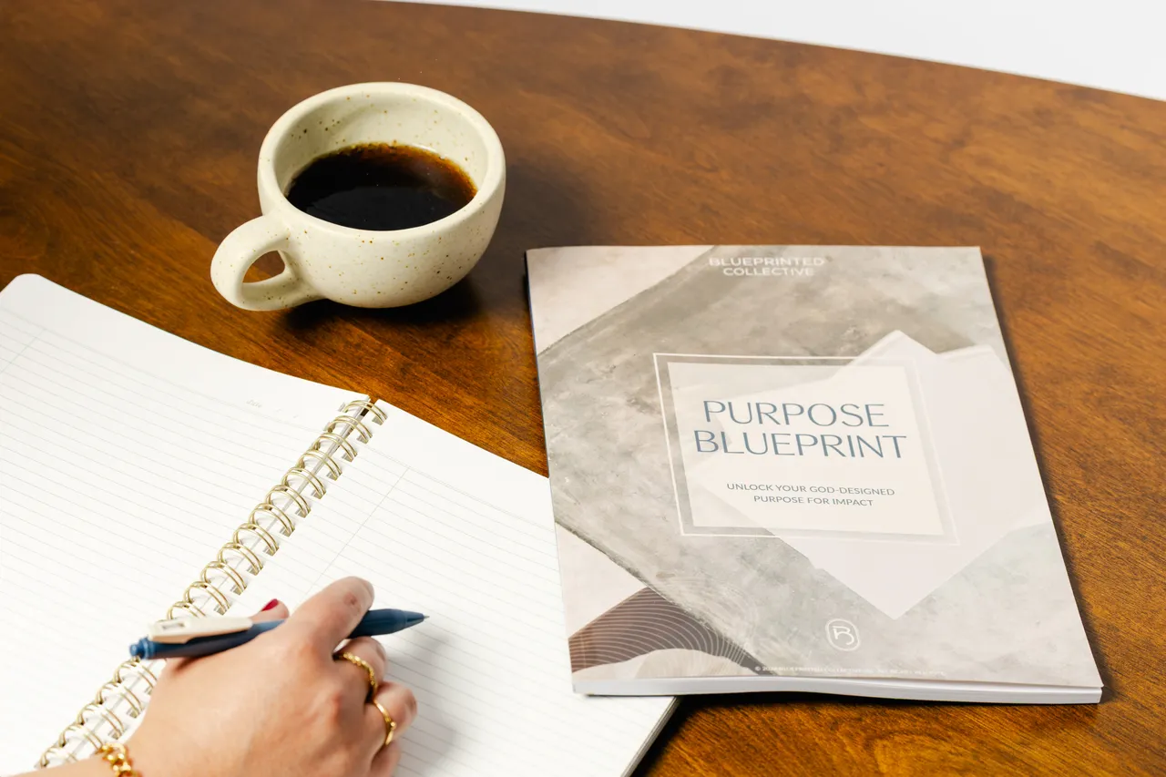 A notebook, coffee, and Purpose Blueprint booklet on a wooden table.